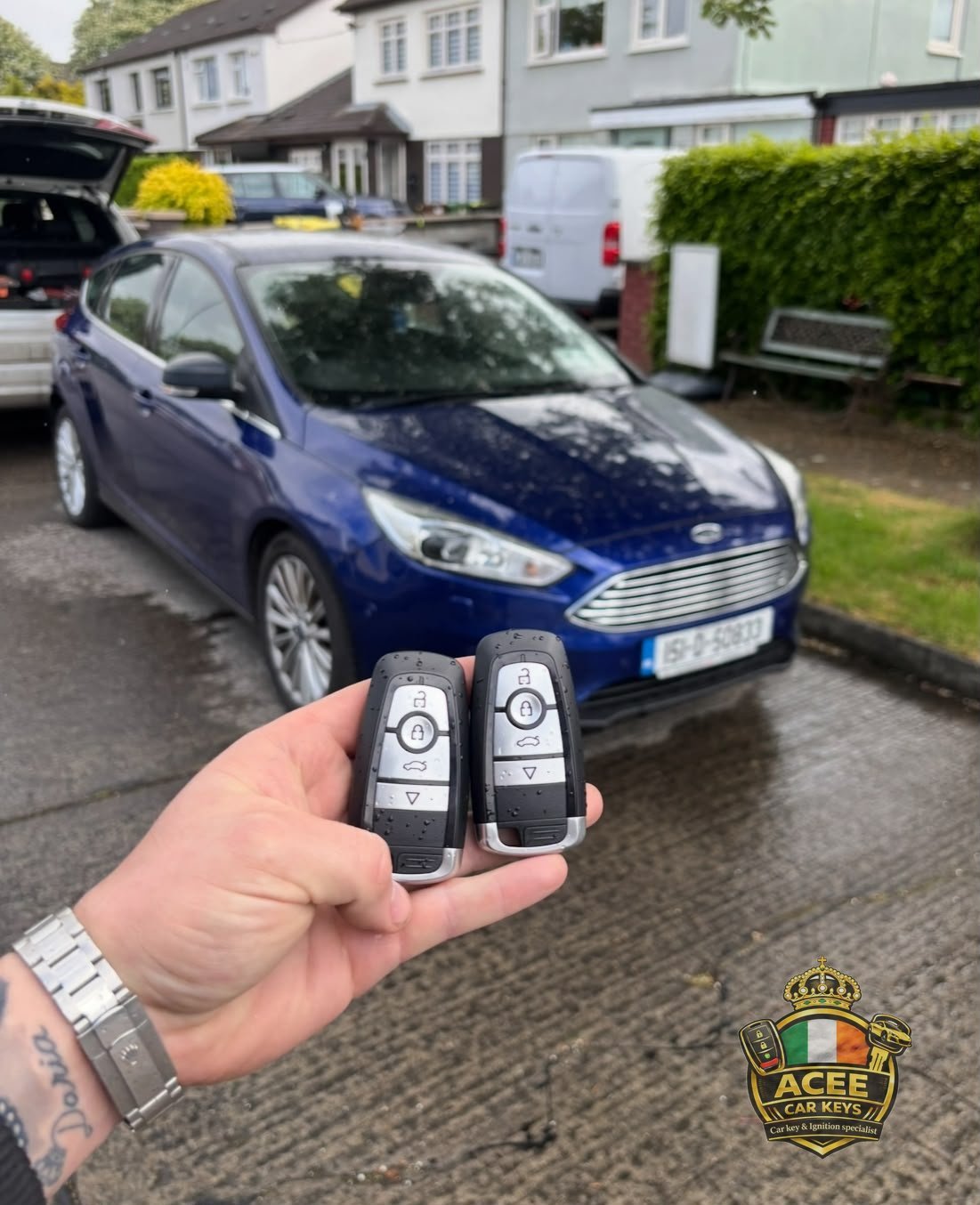 Hand holding two programmed Ford key fobs in front of a blue Ford Focus