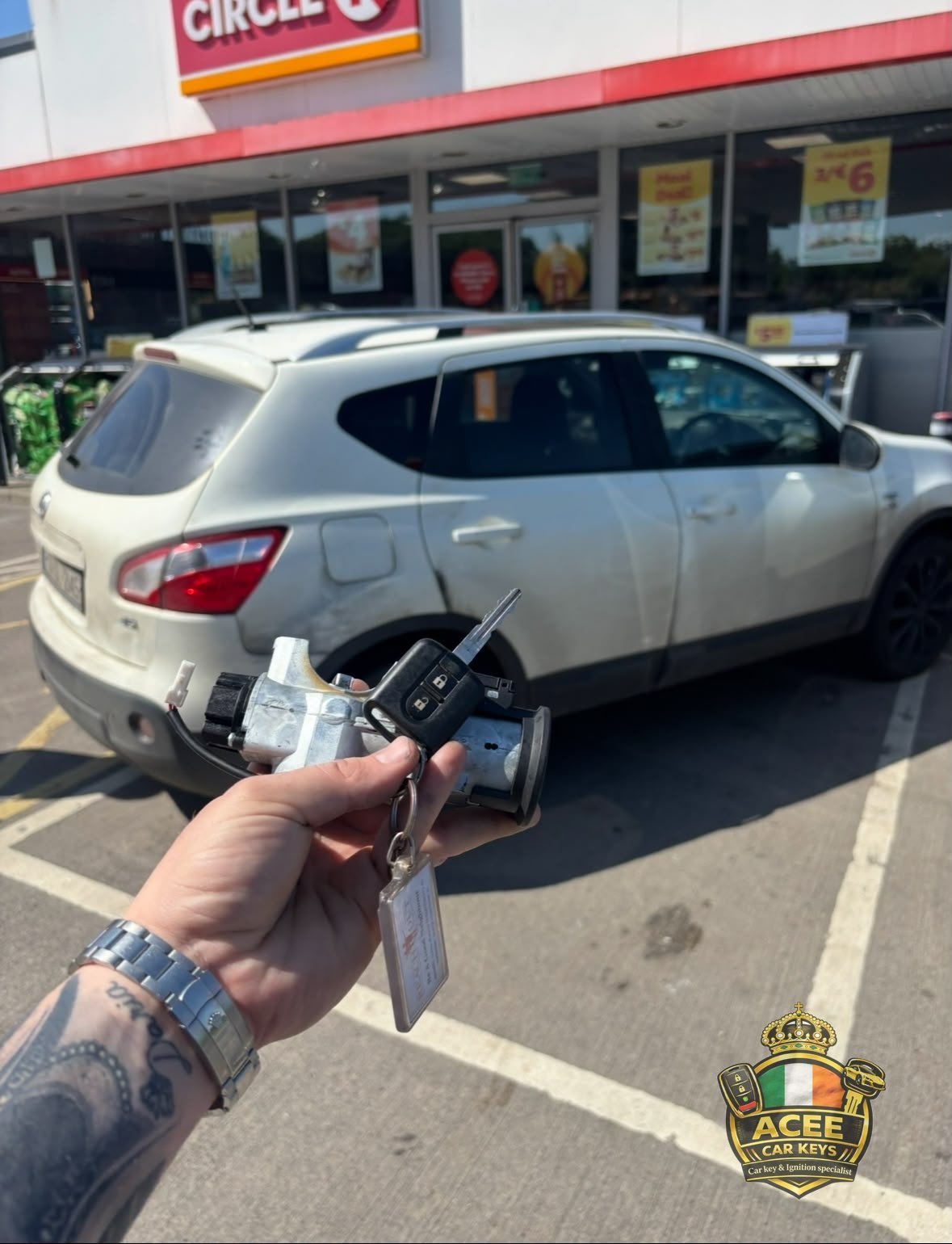 Hand holding car keys and a remote fob in front of a white SUV at a Circle K service station