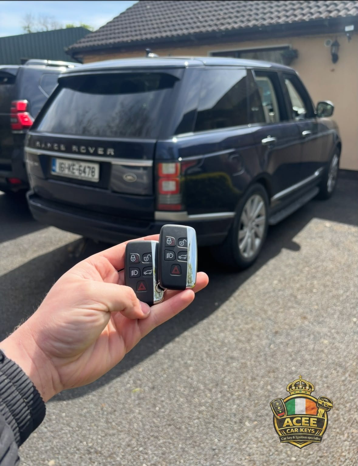 Hand holding a Land Rover key fob with remote controls in front of a dark Range Rover