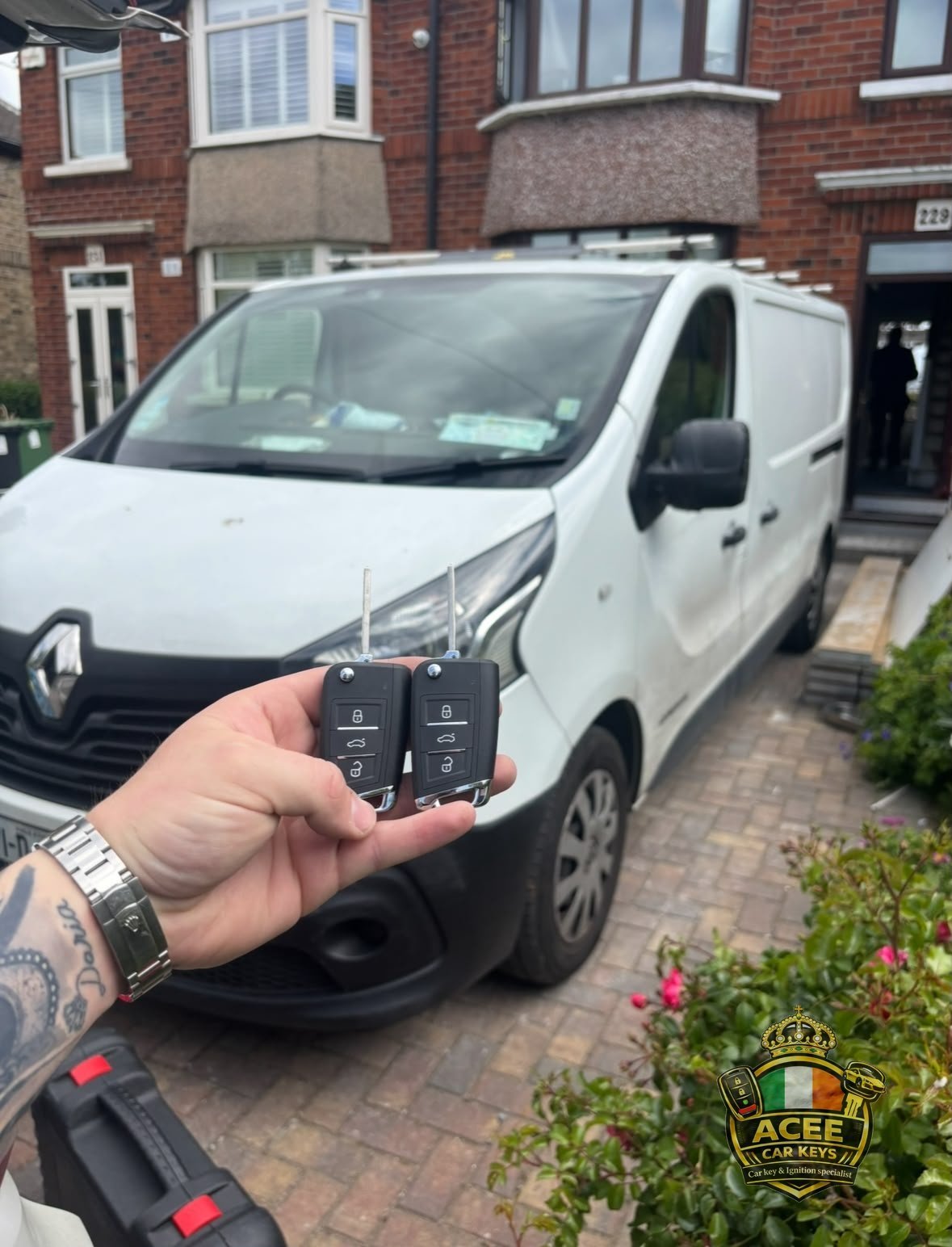 Hand holding a car key fob in front of a white Renault van on a brick driveway