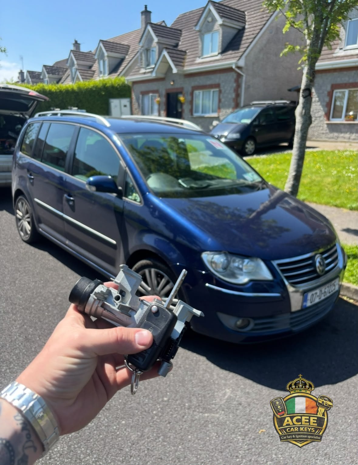 Hand holding car keys in front of a blue Volkswagen Touran in a driveway